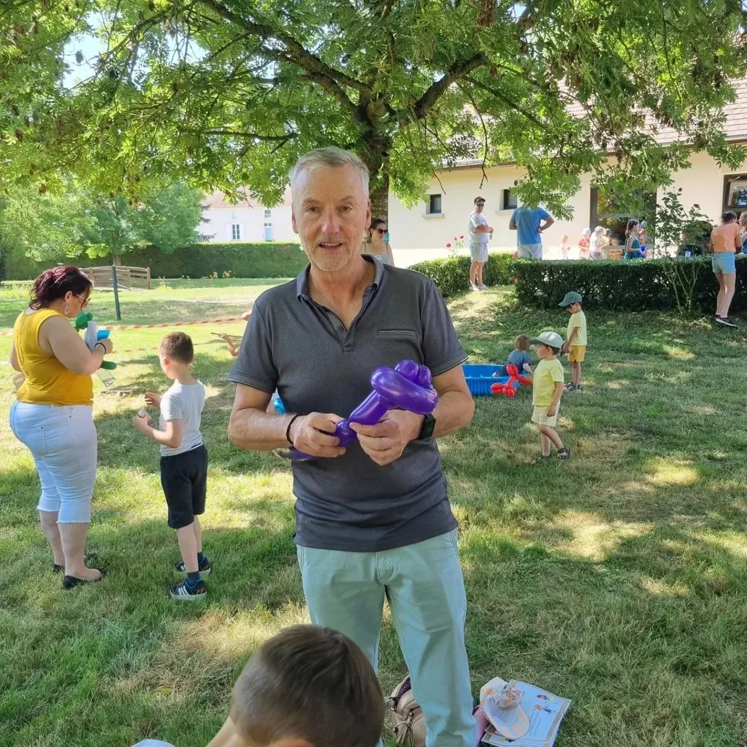 Francis Darcy avec sculpture ballon violet dans un jardin, fête d'enfants en plein air